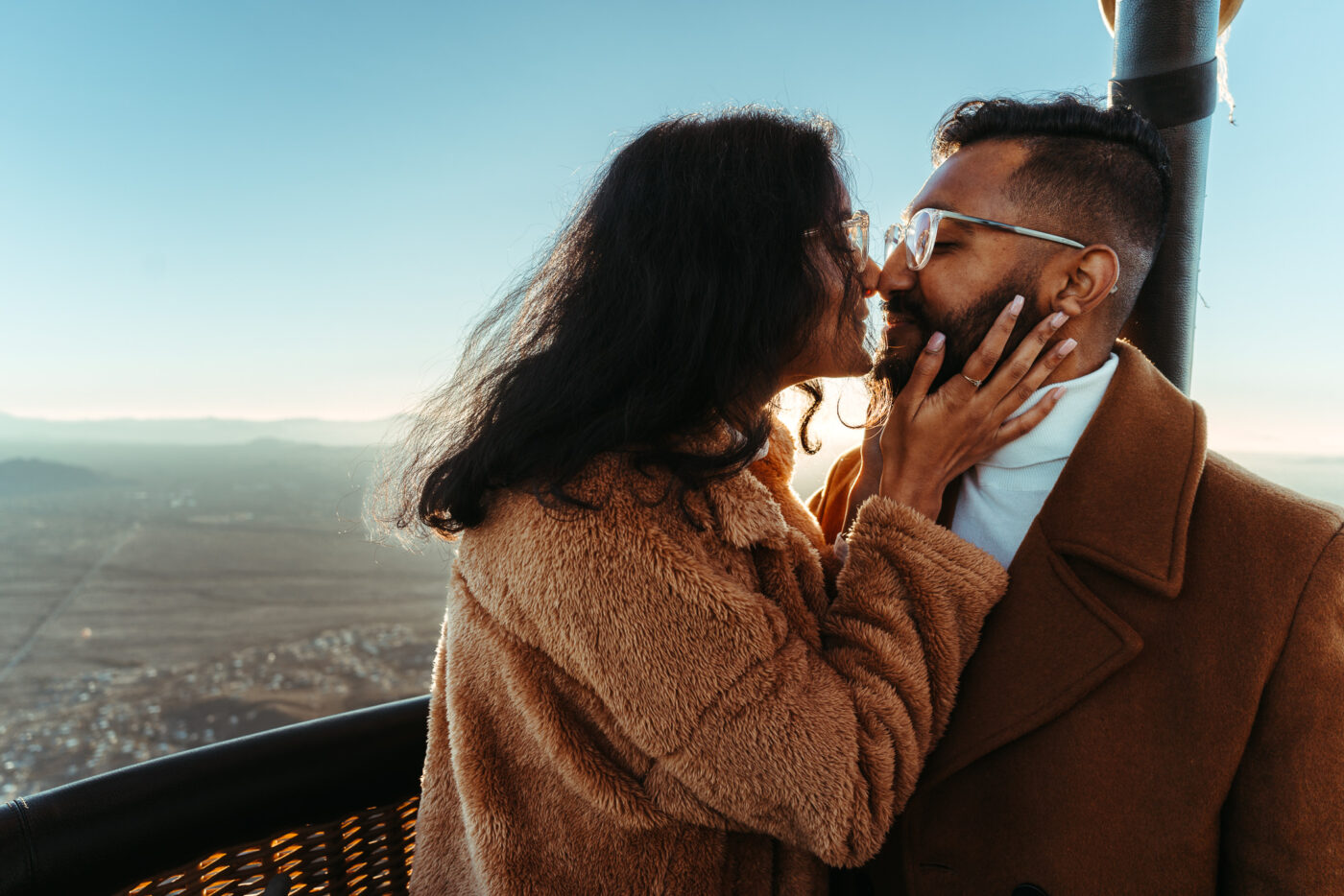 A newly engaged couple about to kiss after a hot air balloon proposal at sunrise over Phoenix, Arizona.